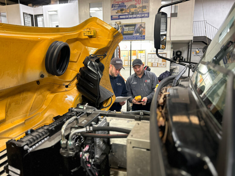 Two technicians looking in the engine compartment of an electric school bus